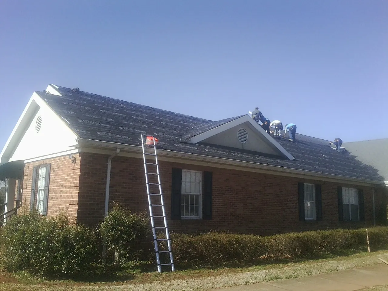 Crew tearing shingles off a brick ranch roof with a ladder set — Emergency Roof Repair work by our crew in Effort