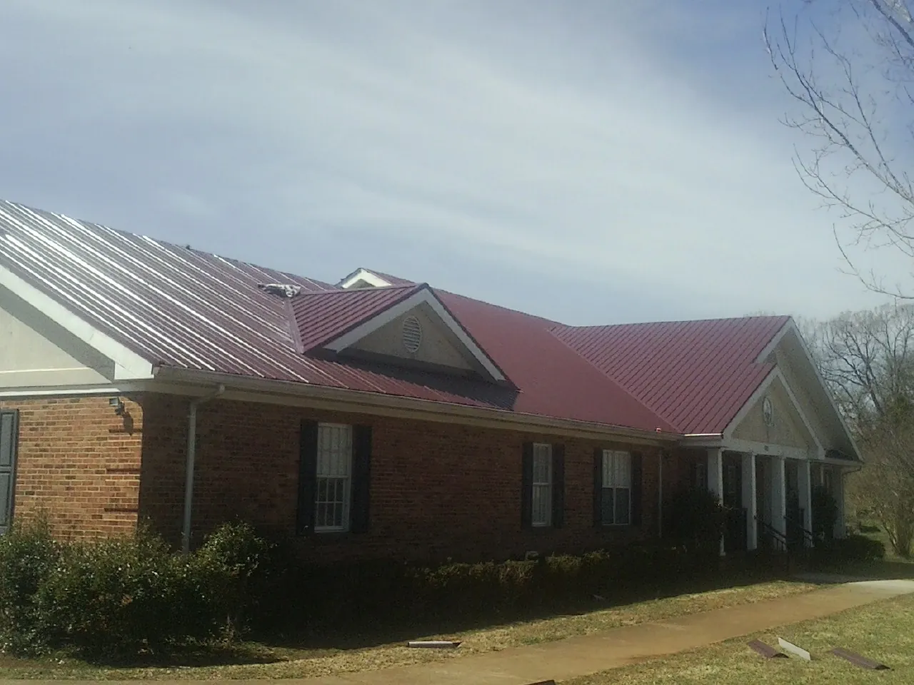 Red metal roof with gabled entries on a long brick building, from a Hail Damage Roof Repair job in Effort