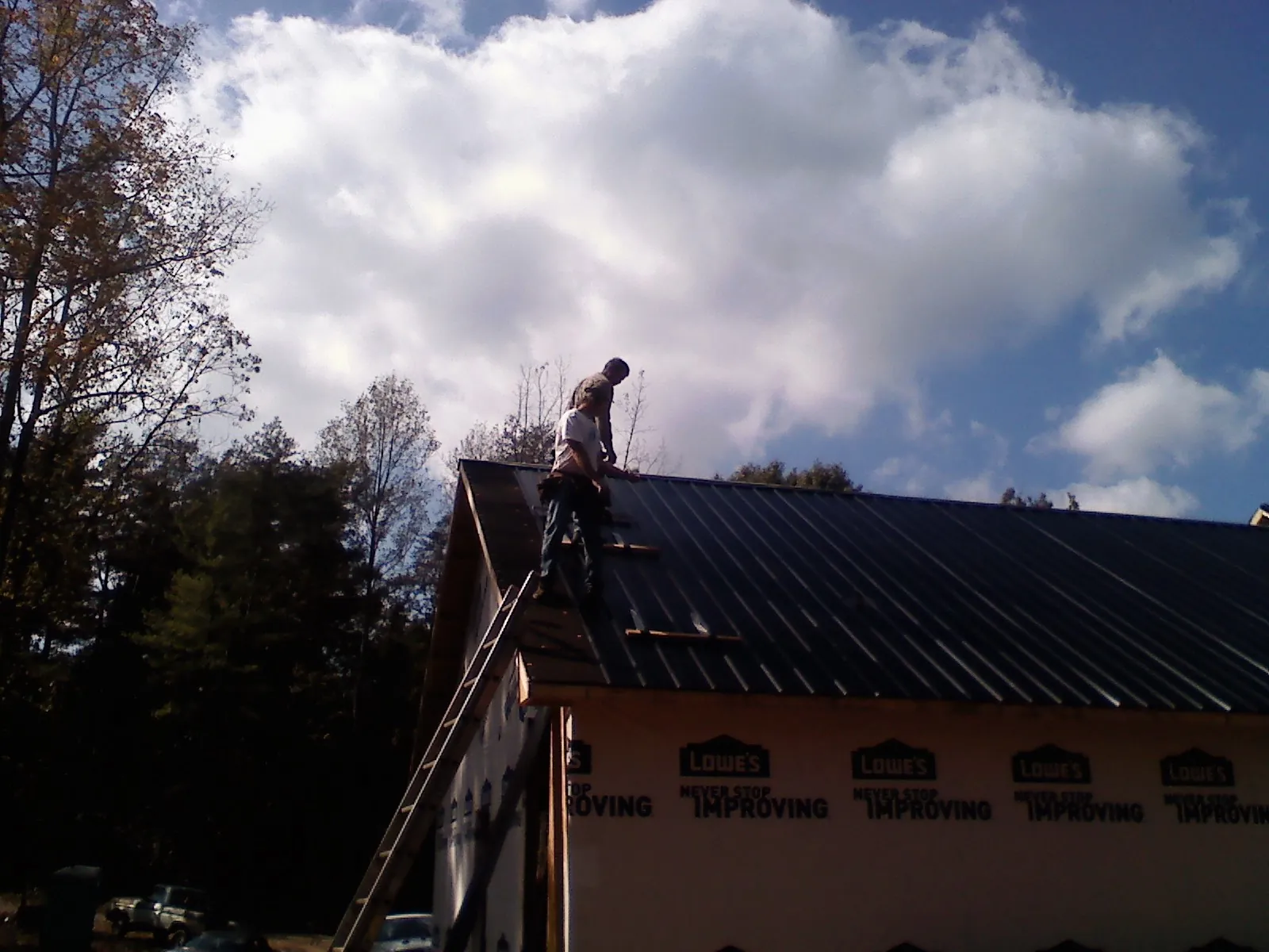 Roofer fastening dark metal panels high against a cloudy sky, from a Roof Inspection job in Effort