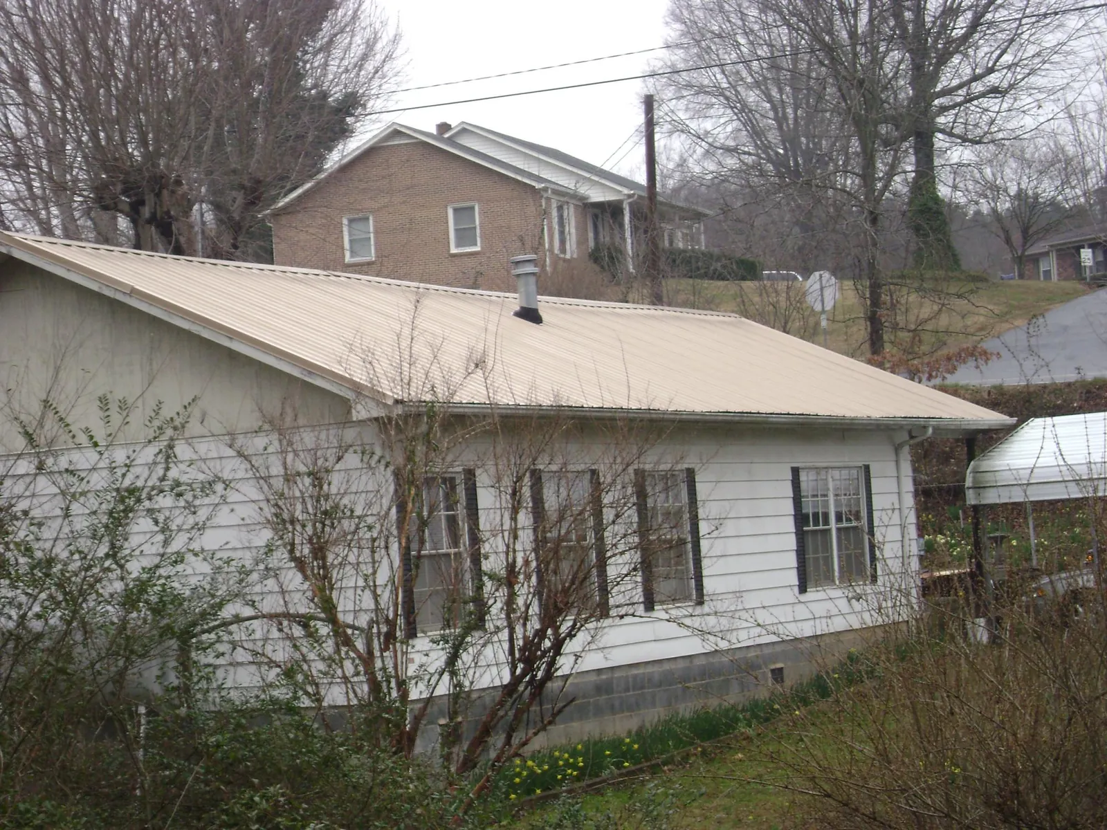 Tan metal roof on a white sided house set into a hillside — Commercial Roofing by Roofing Brothers in Effort
